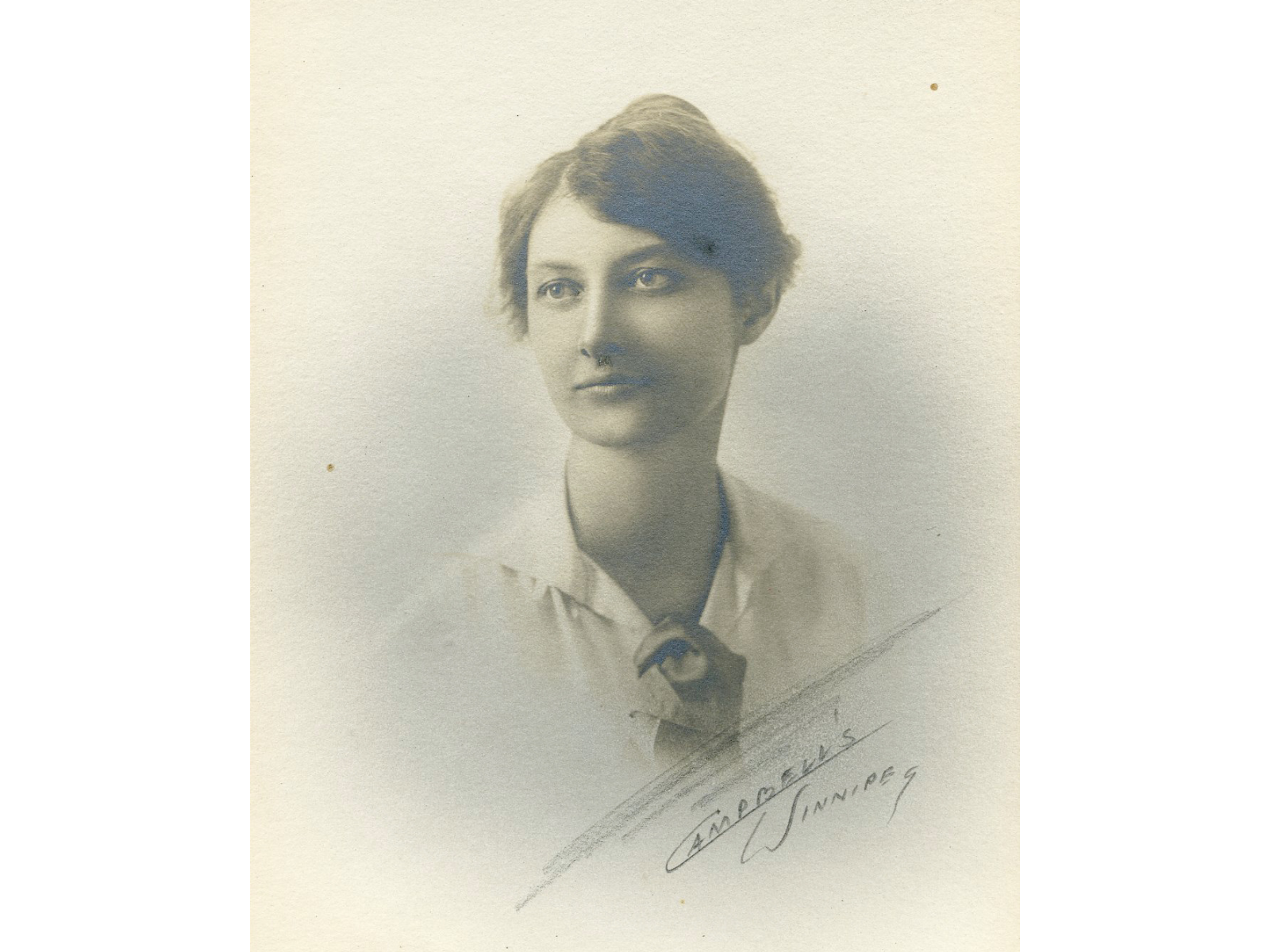 A vintage sepia photograph of a young woman wearing a collared shirt. The image is vignetted in a 3/4 shot. A handwritten signature on the lower right side reads, "Campbell's Winnipeg".