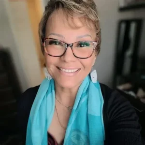 Selfie of artist Dawn Marie Chartrand wearing glasses, a black top, and turquoise scarf, smiling at the camera.