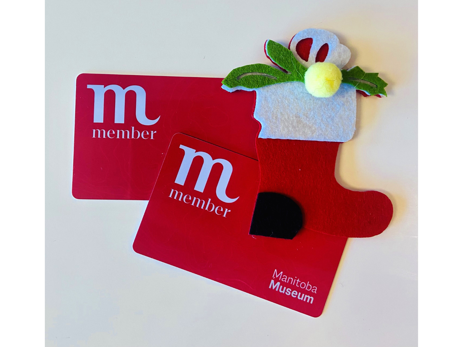 Two red Manitoba Museum Membership cards alongside a red felt stocking decoration.