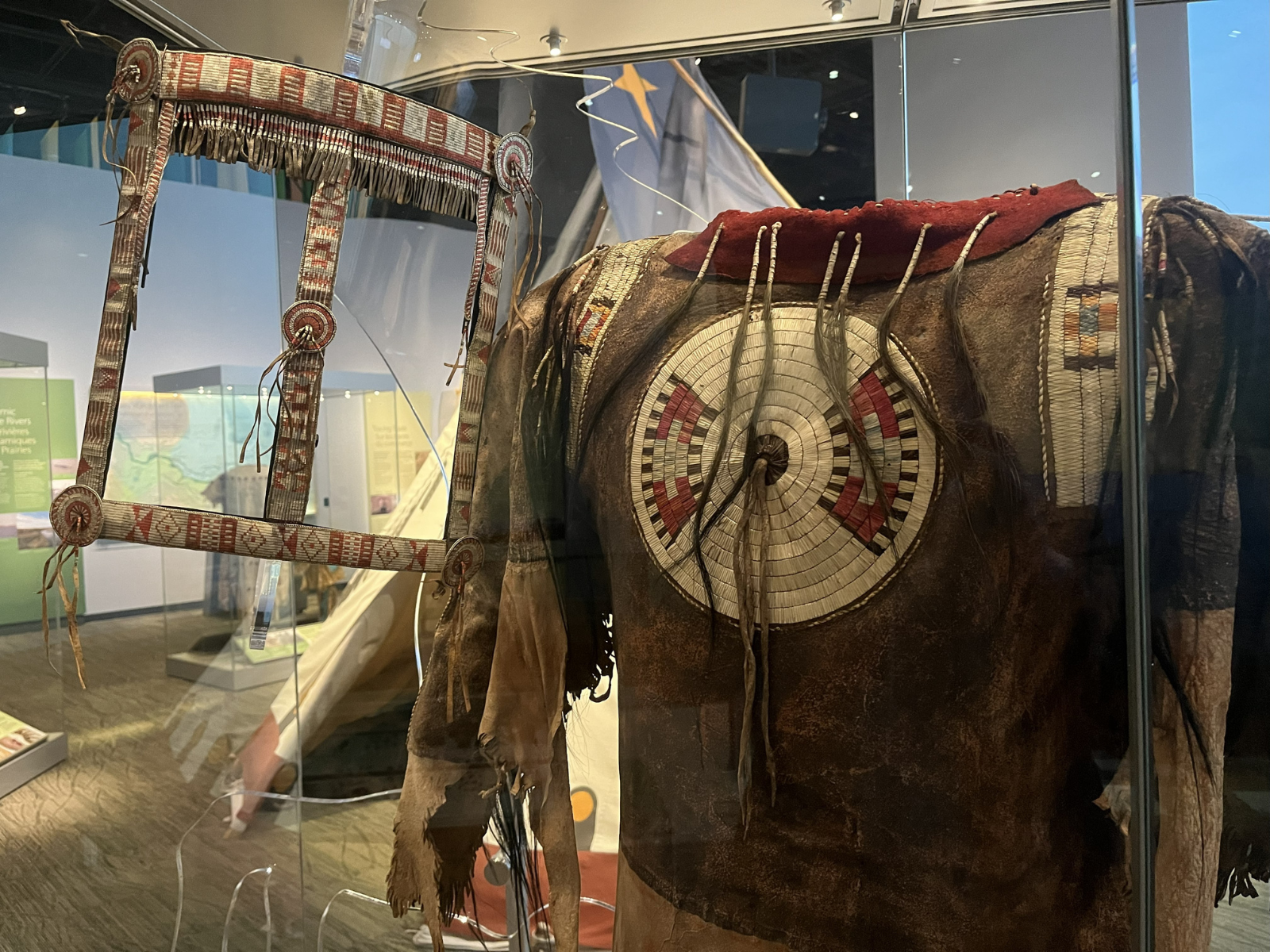 Close-up on a quillwork horse bridle and a shirt with quillwork detailing in a display case in the Prairies Gallery.