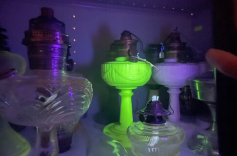 glass lamp bases on a museum collections storage shelf, one of which glows a vibrant yellow-green under a black light.