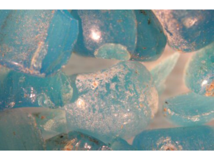 Microscopic image of broken and hazy light blue glass beads.