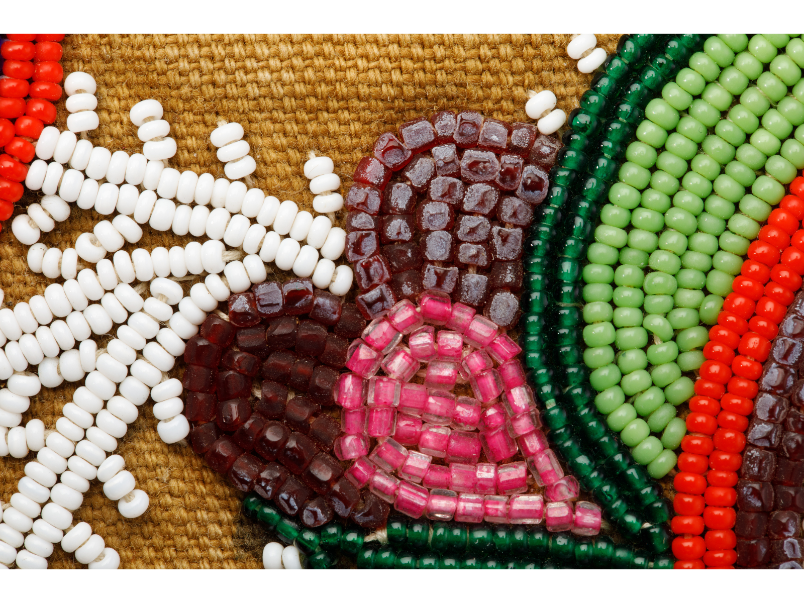 Close-up on a piece of floral beadwork. A section of the beads, particularly a group of purple ones, have taken on a hazy, clouded appearance.