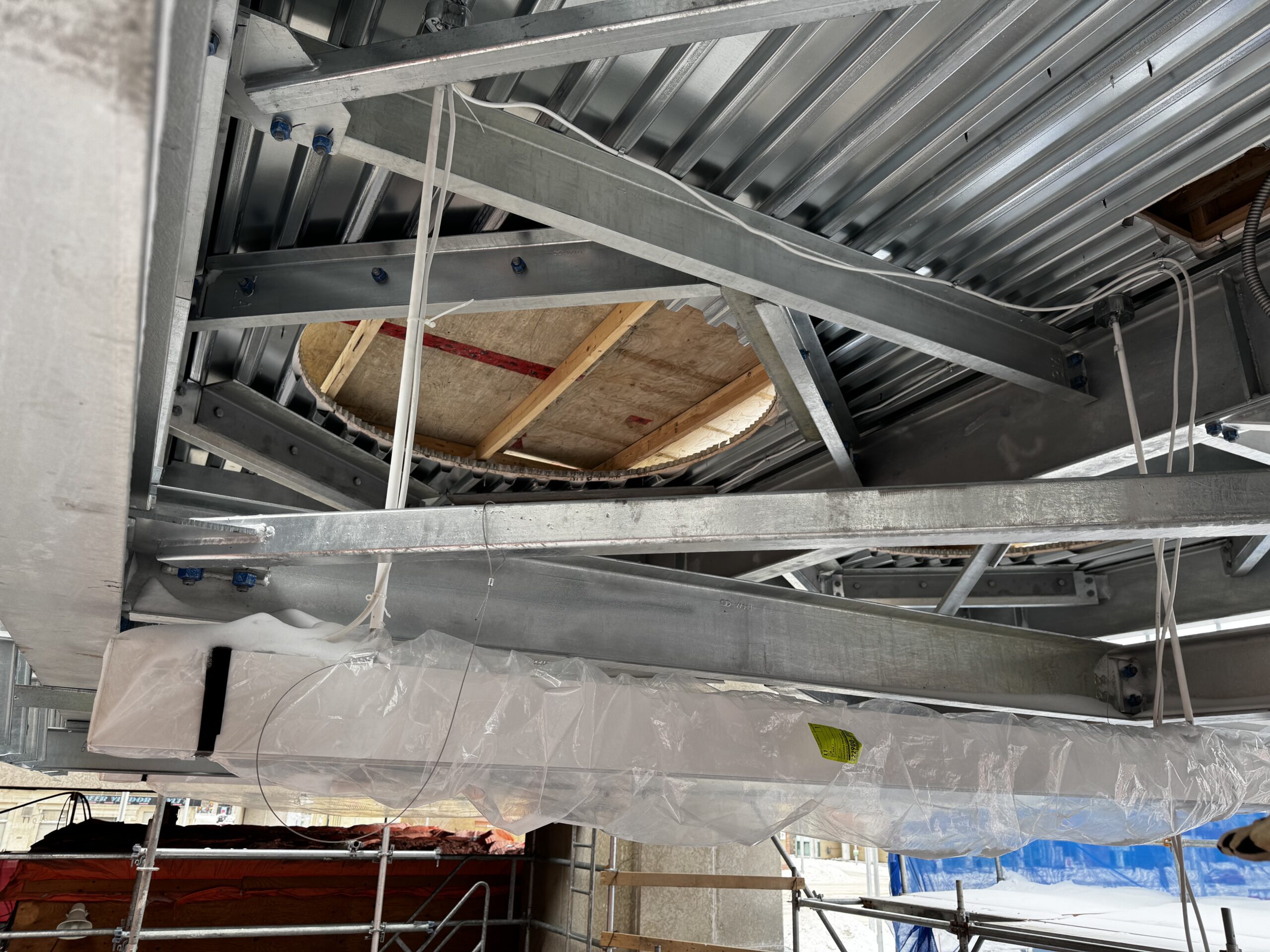 Looking up at a metal framed surface. A circle has been cut out and if covered by wooden boards.