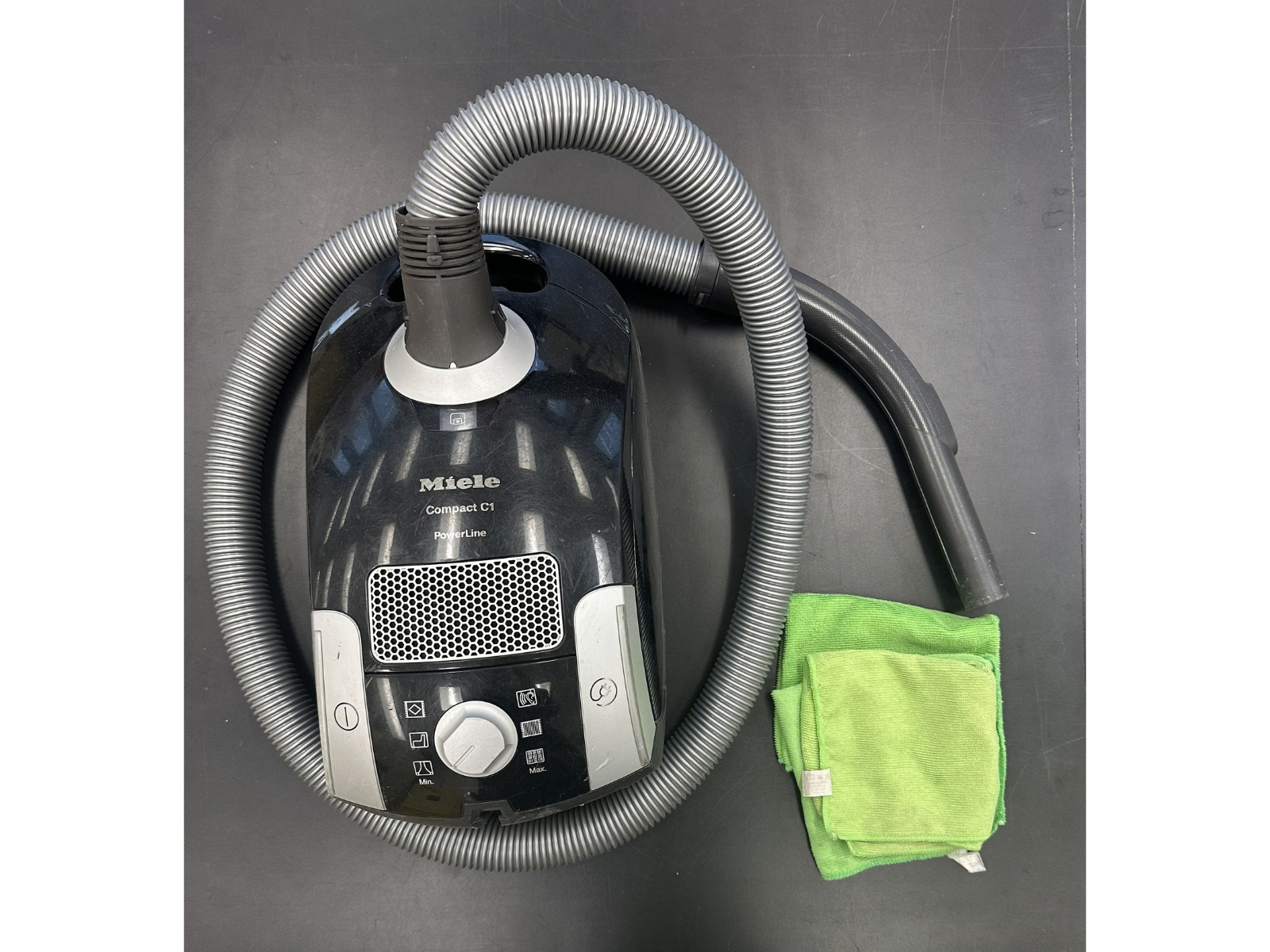Looking down at a canister vacuum wrapped with its hose. Next to it is a neon green microfibre cloth.