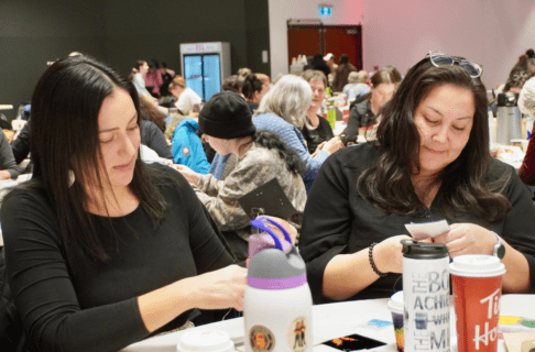 Two beaders seated at a table working on their beadwork projects.