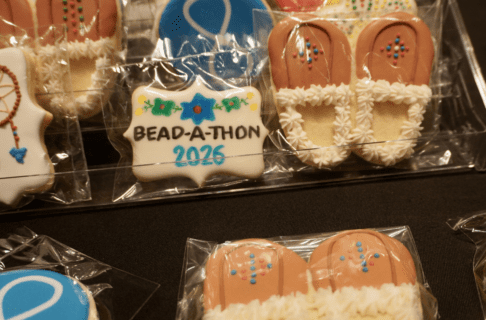 Close-up on intricately iced cookies in designs work moccasins, Métis flags, dream catchers, and words saying "Bead-A-Thon 2026".