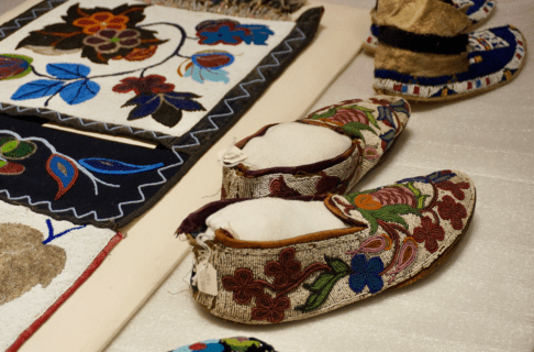 Beaded ancestral belongings on display on a table with an intricate pair of beaded moccasins in the foreground.