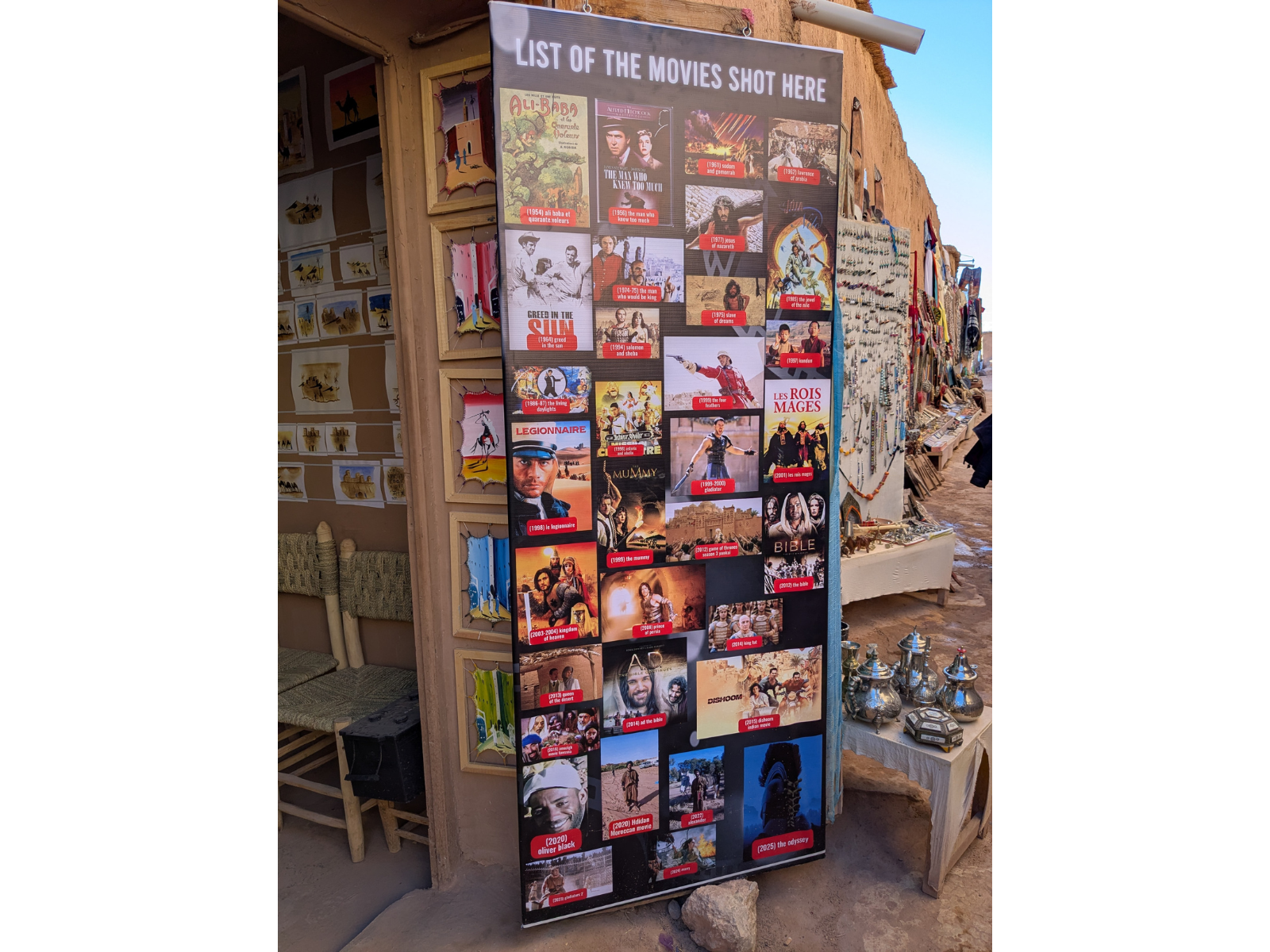 A large banner in front of the entrance to a tan coloured building. Ont he banner are posters and titles of several dozen films and TV show projects filmed at the location.