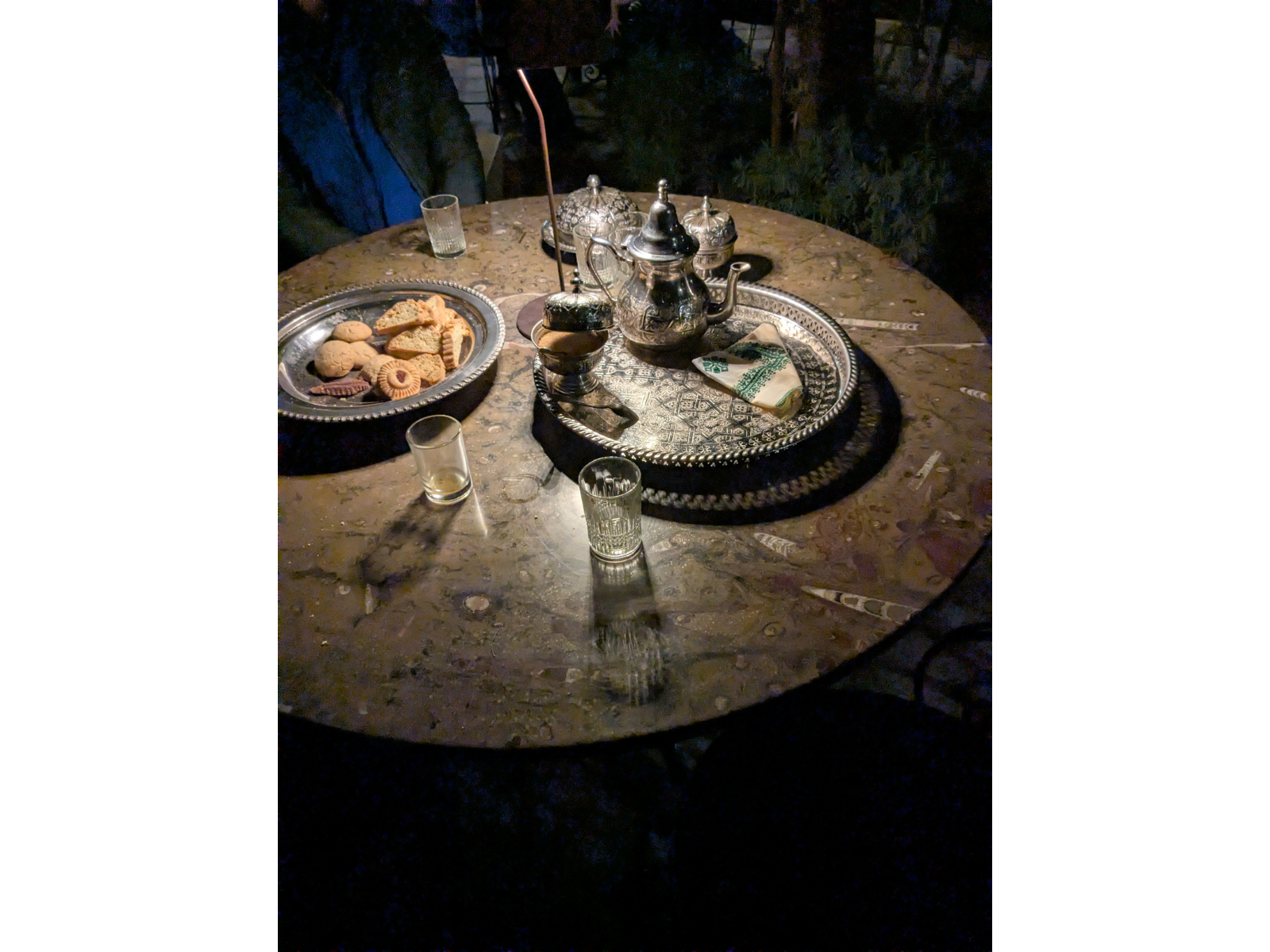 A round table with a variety of fossils in the highly polished limestone. On the table are two trays, one of biscuits the other with a tea set.