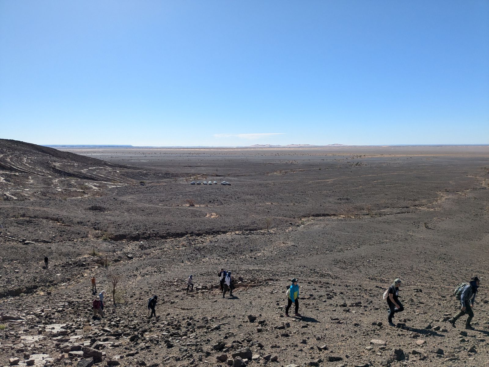 About a dozen people walking along the desert floor in an informal line.