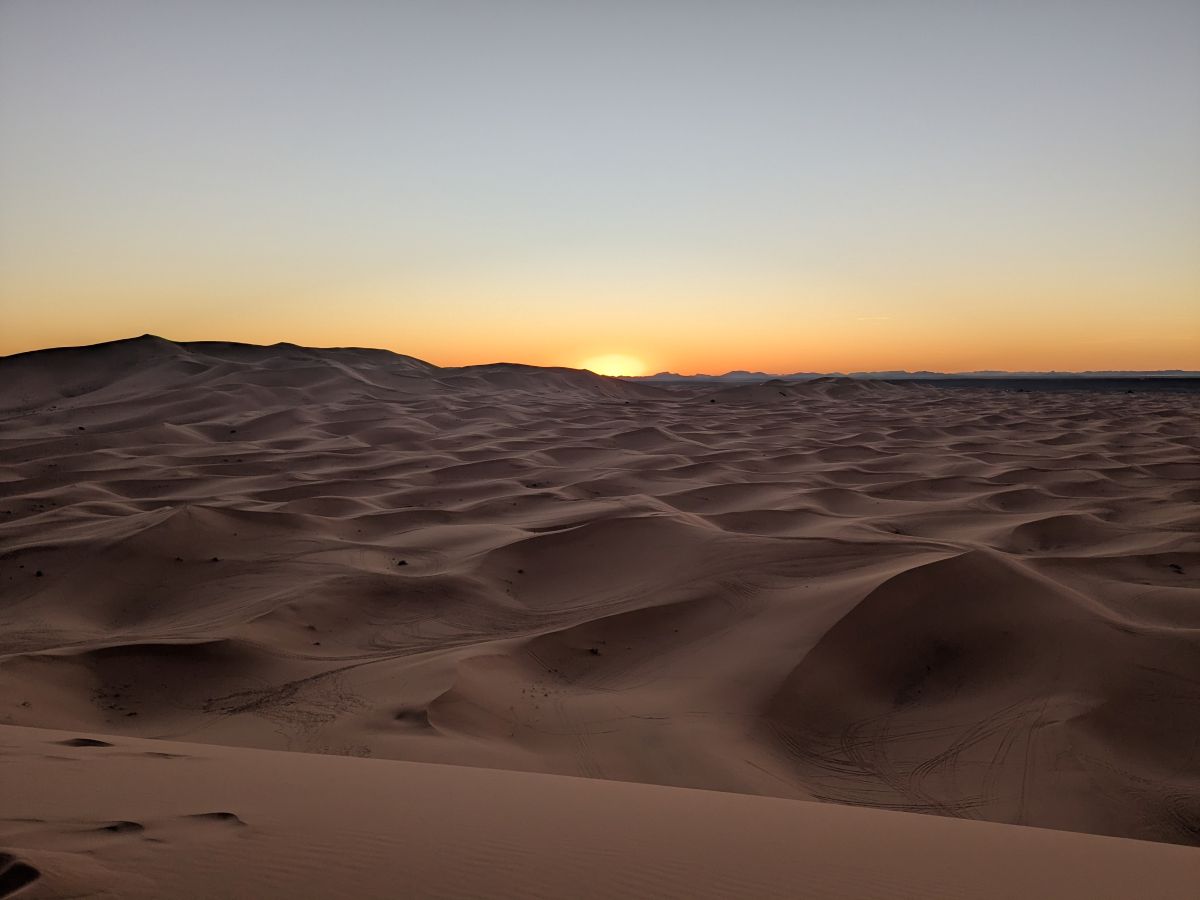 A sunset over an expense of undulating sand dunes.