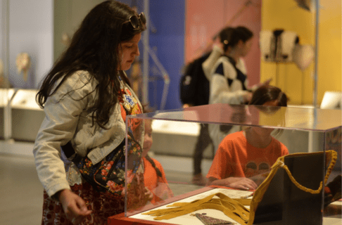 An adult and two children wearing orange shirts look at artifacts displayed in a case in the Welcome Gallery.