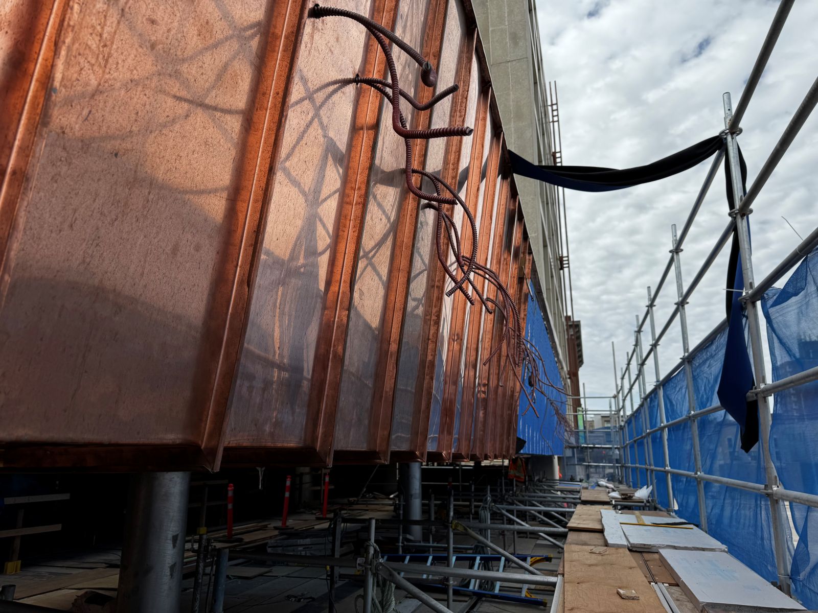 Along the left, cables sticking out of copper cladding art regular intervals. Scaffolding and tarpaulin barriers on the right.