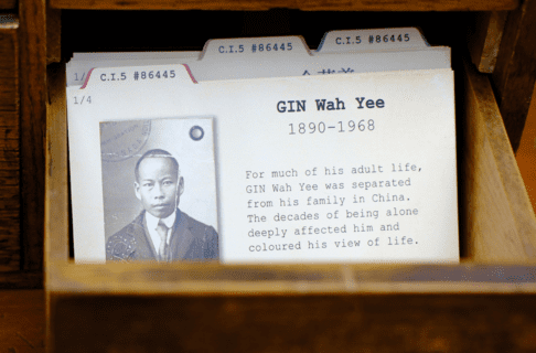 A small open drawer containing index cards, the front of which has a black and white documentation photo of a Chinese Canadian man, identified at GIN Wah Yee (1890-1968).