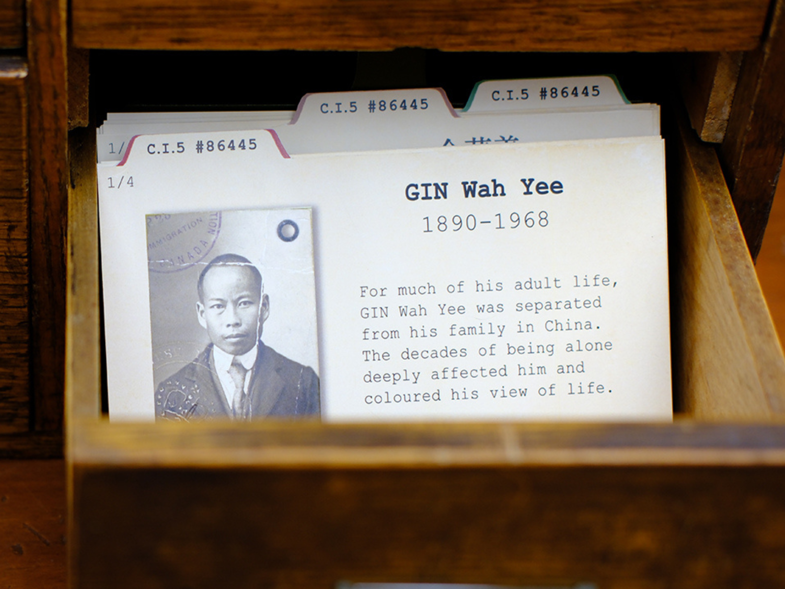 A small open drawer containing index cards, the front of which has a black and white documentation photo of a Chinese Canadian man, identified at GIN Wah Yee (1890-1968).