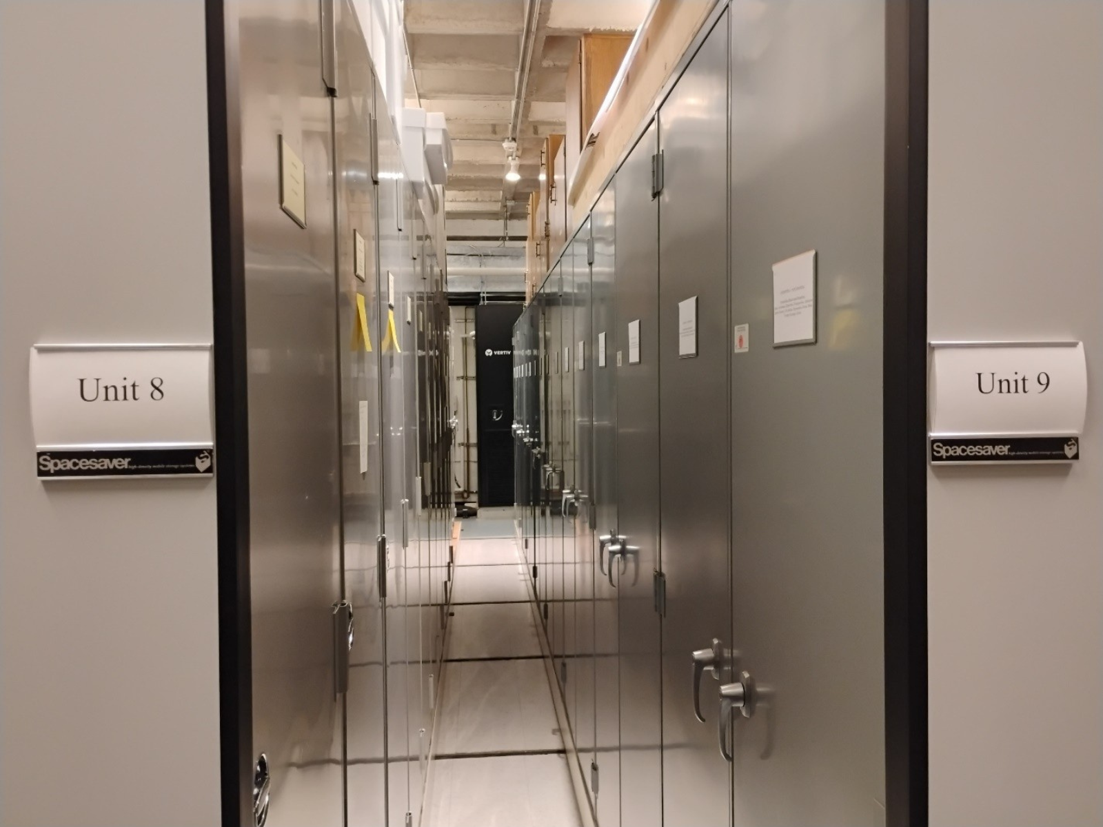 Looking down the aisle between two rolling units of storage cabinets. On the outer sides, closest to the camera, labels read "Unit 8" and "Unit 9".